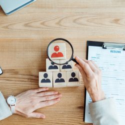 top view of recruiter holding magnifier near cube and clipboard in office